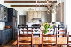 a dining room table and chairs in front of a kitchen with blue cabinets, wood floors and wooden beams