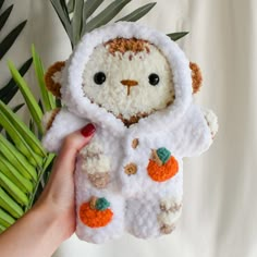 a hand holding a small stuffed animal in a white coat with oranges on it