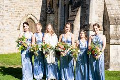 a group of women standing next to each other in front of a stone building holding bouquets