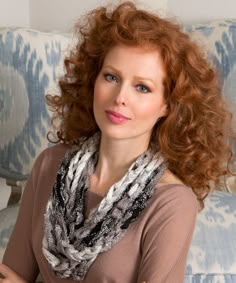 a woman with red hair is sitting on a blue and white couch wearing a scarf