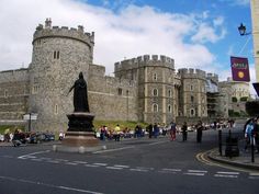 people are standing in front of an old castle with a statue on the side walk