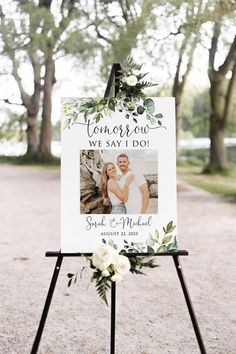 a wedding sign with flowers and greenery is displayed on a easel in front of trees