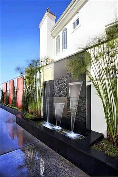 an outdoor water feature in front of a house with grass and plants on the side