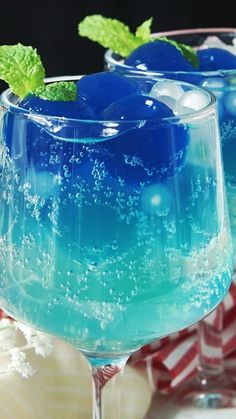 two glasses filled with blue liquid and mint garnish on top of a table