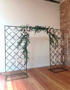 an arch with flowers and greenery on it in the middle of a wooden floor