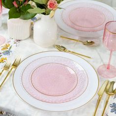 the table is set with pink plates and goldware