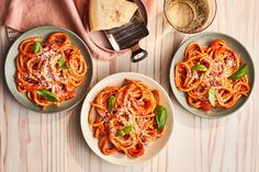 three plates of spaghetti with basil and parmesan cheese on top, next to a glass of wine