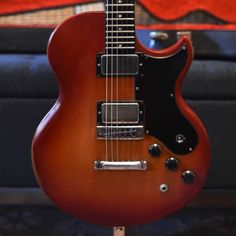 a red electric guitar sitting on top of a wooden stand in front of a couch