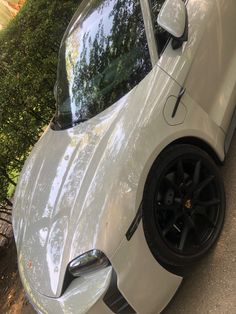 a white sports car parked on the side of the road next to some bushes and trees