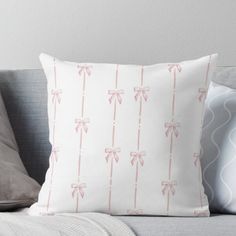 a white pillow with pink bows on it sitting on a gray couch next to pillows