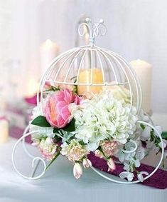 a white birdcage filled with flowers on top of a table next to candles