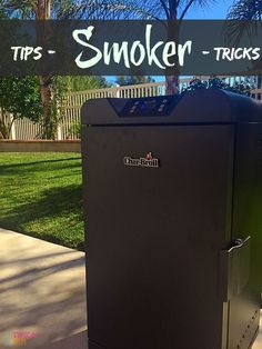 a black smoker sitting on top of a sidewalk next to a green lawn and palm tree