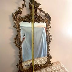 an ornate gold mirror is hanging on the wall next to a bed with a sheet draped over it