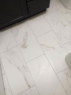 a bathroom with a toilet, sink and cabinets in the background is white marble tile