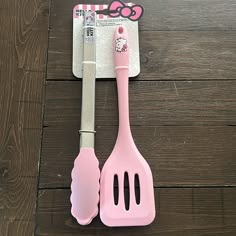 two pink utensils sitting next to each other on a wooden surface with hello kitty stickers