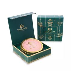 an open box with a gold lid and pink wax in it on a white background