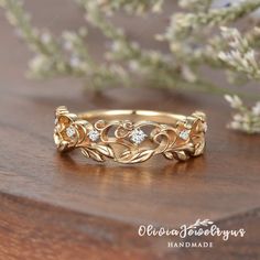 a gold wedding band with three diamonds on the side and leaves in the middle, sitting on top of a wooden table