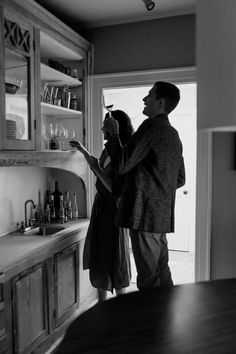 a man and woman are standing in the kitchen looking at each other's wine glasses