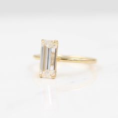 an emerald - cut diamond ring sits on a white surface