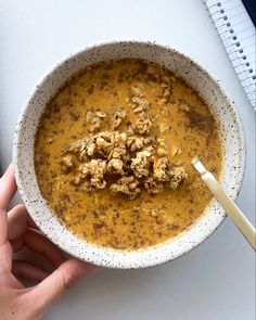 a person holding a bowl of soup on top of a white table next to a notebook