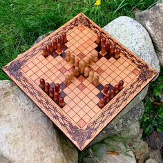 a wooden chess set sitting on top of a stone slab next to grass and rocks