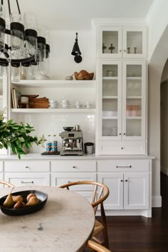 a kitchen with white cabinets and wooden floors, an oval dining table in the center