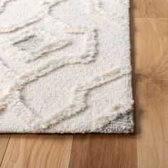 a white rug on the floor with wood floors in the background and an area rug that has fringed edges