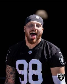 a man with a beard wearing a football uniform and making a funny face while standing in front of a black background