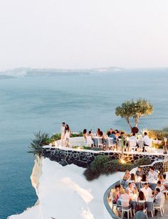 a group of people sitting at tables on top of a cliff next to the ocean