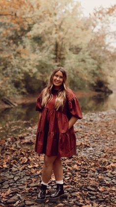 a woman in a red dress and black boots posing for a photo by the river