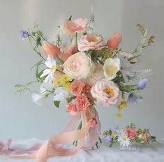 a bouquet of flowers is sitting on a table with ribbon around the vase and ribbons in front of it