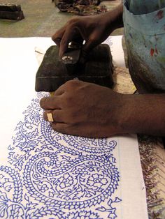 a person using a machine to cut fabric on a piece of paper with blue and white designs