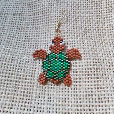 a green and red beaded turtle sitting on top of a white cloth