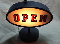 an open sign is lit up on a black stand with a white sheet behind it