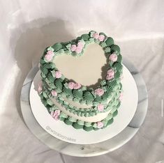 a heart shaped cake with green frosting and pink flowers on top, sitting on a white plate