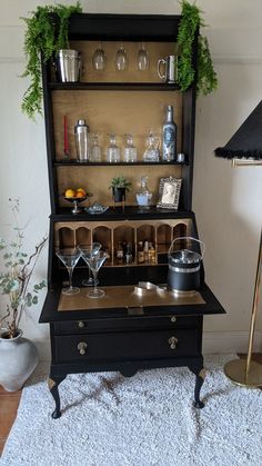 an old fashioned black cabinet with wine glasses and cups on it's top shelf