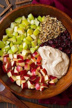 a wooden bowl filled with apples, raisins and other toppings on top of a table