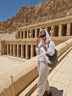 a woman standing in front of an ancient temple with her cell phone to her ear