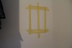 a piece of yellow tape is taped to the side of a white wall with a black coat hanging on it