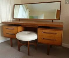 a mirror sitting on top of a wooden dresser next to a white footstool