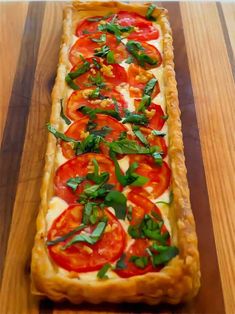 a long rectangular pizza with tomatoes and basil on top, sitting on a wooden surface