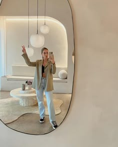 a woman taking a selfie in front of a mirror with lights hanging from the ceiling