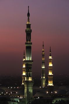 two tall towers lit up at night with lights on them and buildings in the background