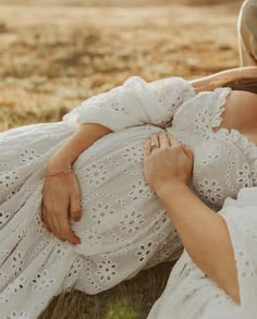 a pregnant woman in a white dress laying on the ground next to a man wearing a cowboy hat