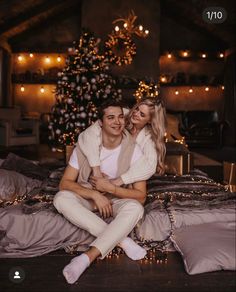 a man and woman sitting on top of a bed in front of a christmas tree