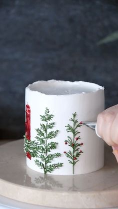 someone is using a knife to decorate a cup on a plate with holly and red berries