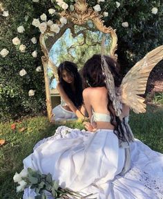 two women sitting in front of a mirror with angel wings on their backs and flowers around them