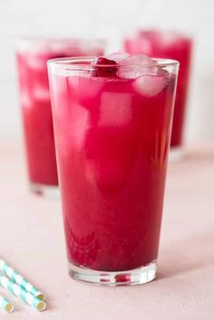 two glasses filled with red liquid next to straws