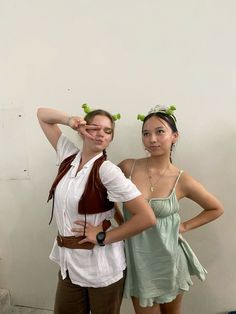 two young women standing next to each other in front of a white wall wearing costumes