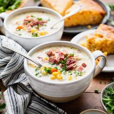 two bowls of soup with corn and ham in them on a wooden table next to bread